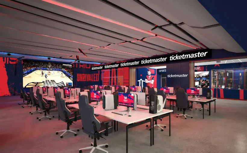 Interior view of an esports gaming room with rows of tables and monitors plus large TV screens on the walls