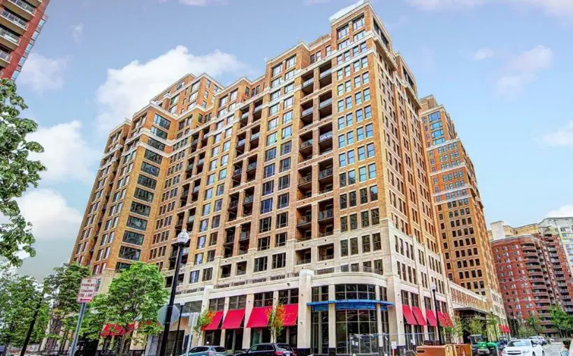 Exterior view of 19-story apartment building with awnings over the sidewalk and ground-floor shops.