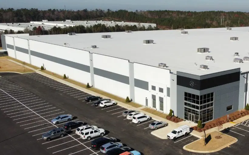 Aerial view of parking lot and large industrial building with a corner entrance and the Mercedes logo over the door