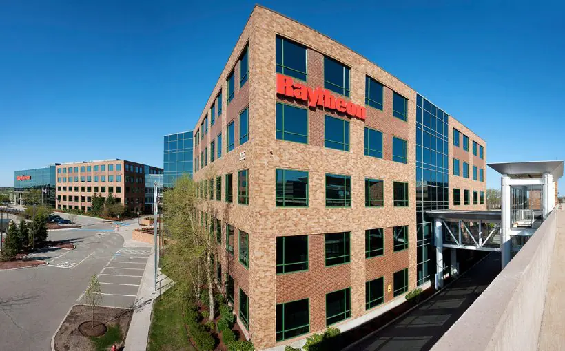 Long range exterior view of two large mid rise brick and glass buildings with the closer situated next to a rail depot