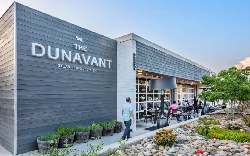 Modernized single-story commercial building with weathered wood paneling and outdoor restaurant seating and rock garden