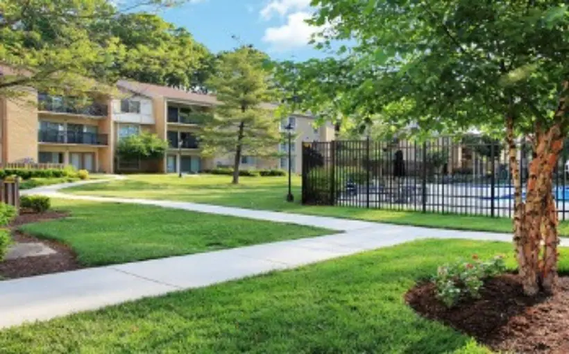 Exterior view of three-story apartment complex with back balconies overlooking a fenced-in pool and greenspace