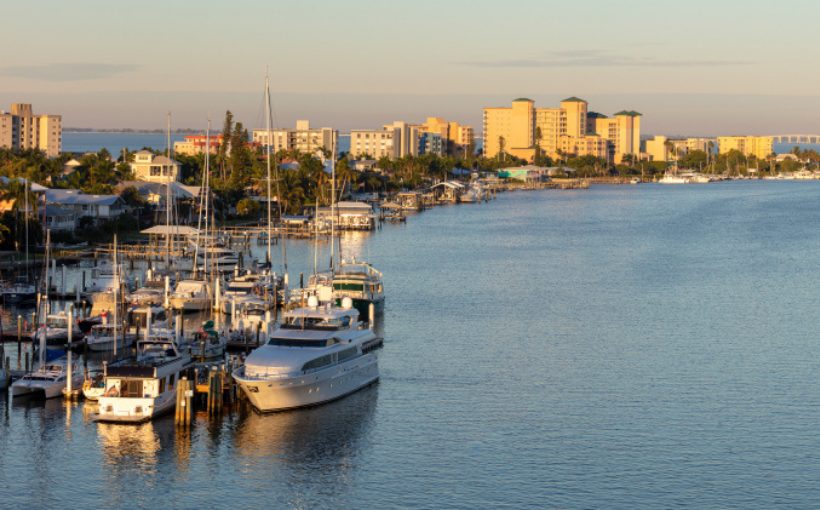Long range view of docked yachts and a curving coastline with buildings leading to a downtown skyline
