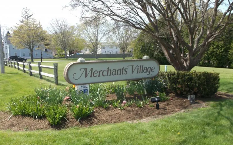 Apartment complex ground sign on a small grassy hill with trees and two-story buildings in the background