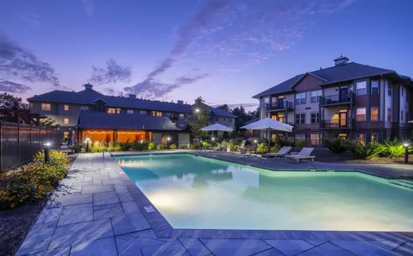 Poolside view of three-story building with balconies along with lounging cabanas at twilight