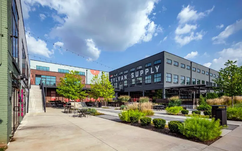 Exterior view of a courtyard with tables and chairs surrounded by low urban office buildings