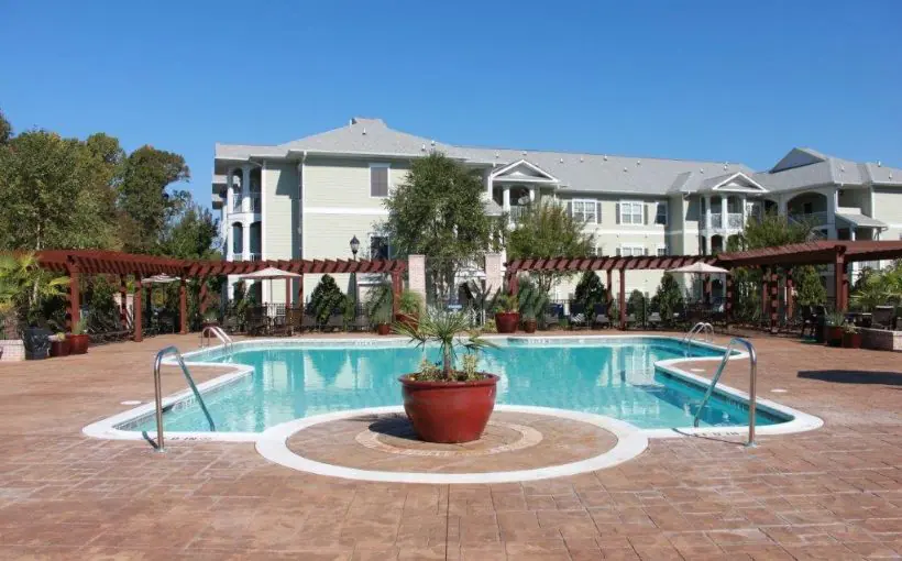 Exterior view of two-story apartment building overlooking pool and lounging area