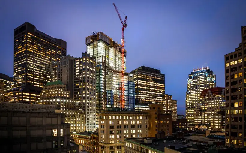 Mid range exterior view of a group of downtown Boston buildings at twilight, along with an enormous construction crane in front of the center building