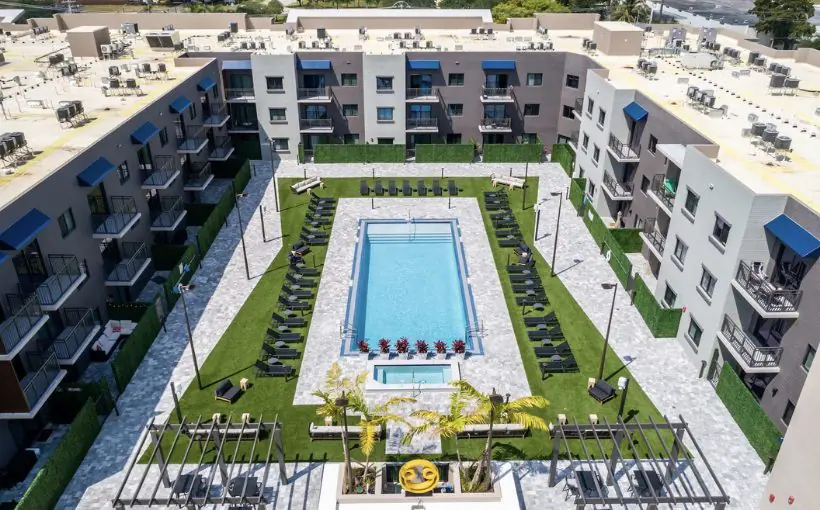 Aerial view of a three-story horseshoe shaped apartment building with windows and balconies surrounding the pool and lounge area