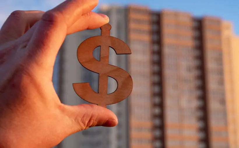 Hand holding wooden dollar against apartment